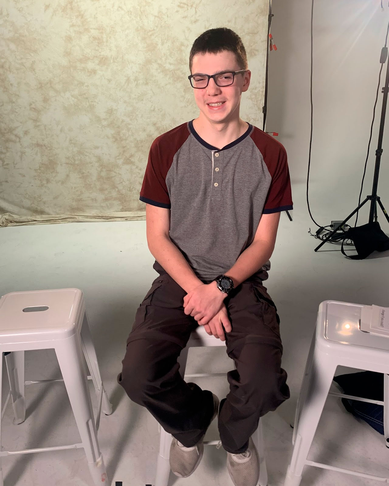 A photo of Curtis sitting on a stool looking into the camera and smiling.