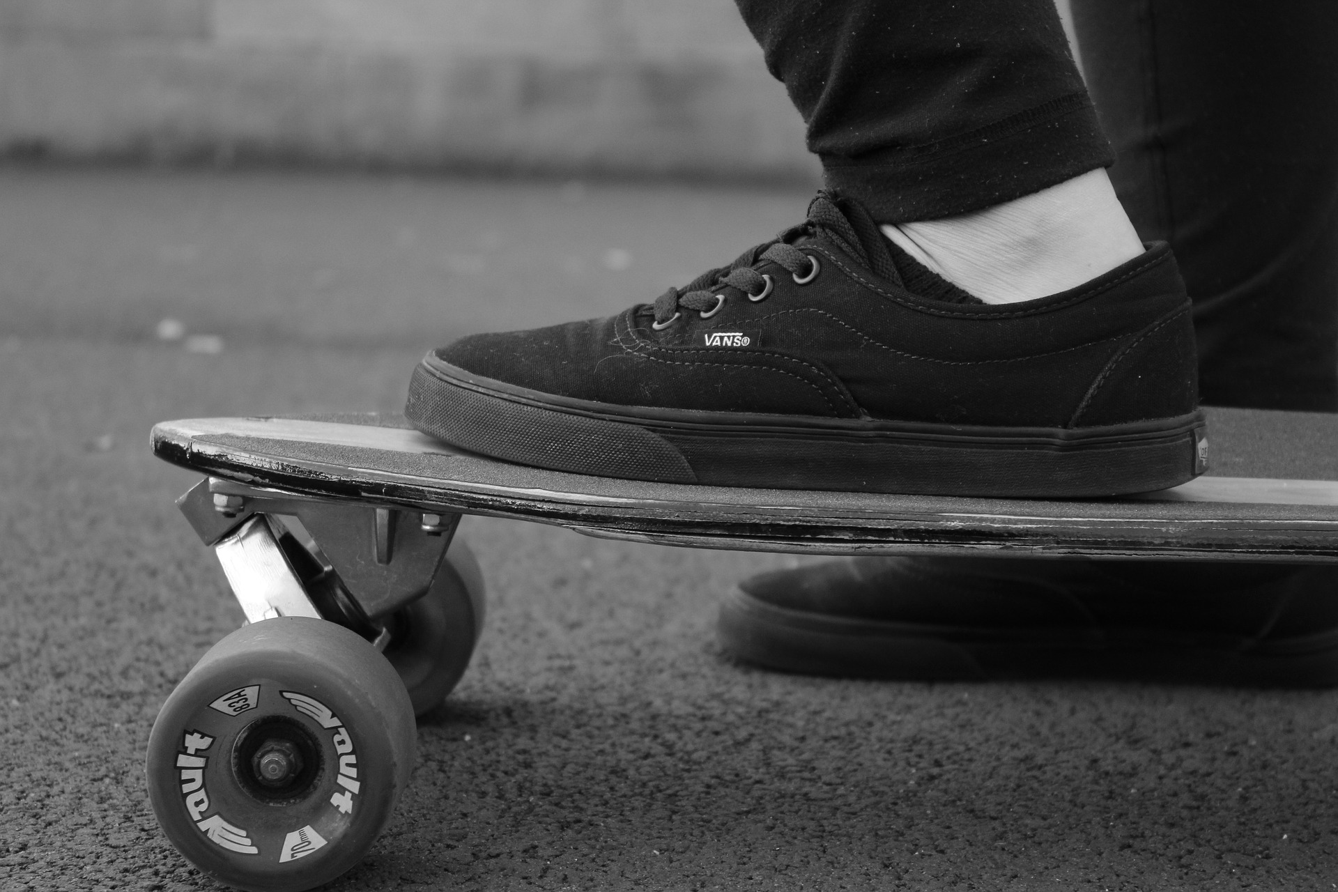 black and white photo of a person wearing black skate shoes one foot on a skateboar, the other foot on the ground.