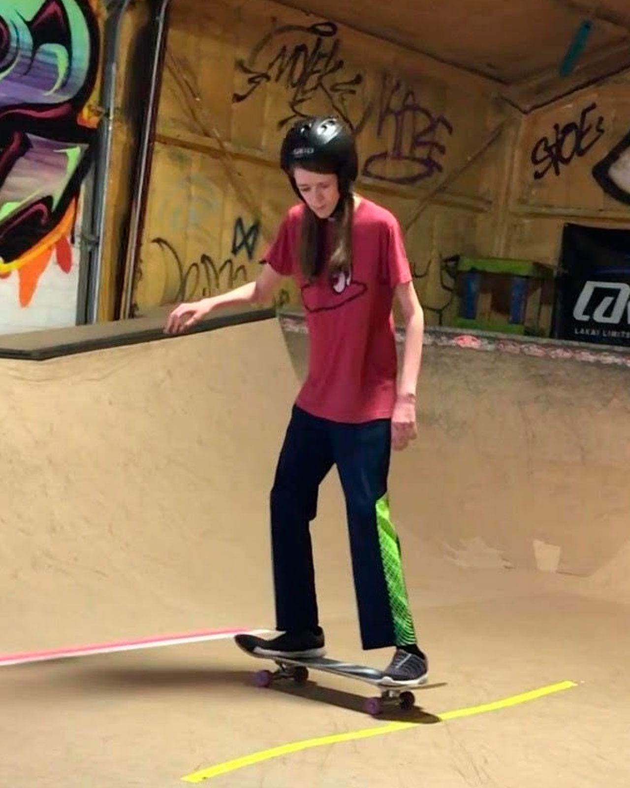 Zach standing on a skateboard, Zach is looking down at his feet, and has his arms out to his side for balance.